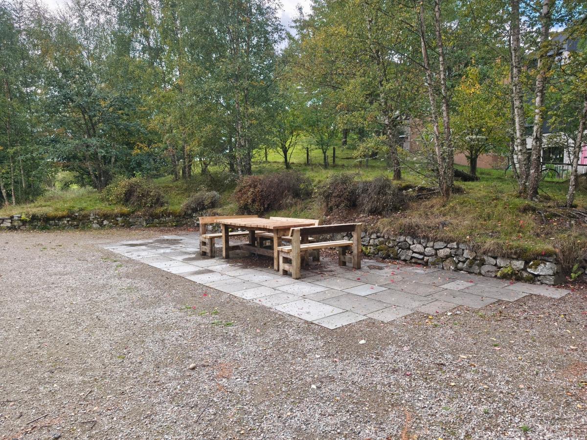 Picnic table and three benches on slabbed ground.