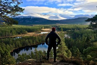 Person looking down at Uath Lochans with forests and snowy mountains in the distance.