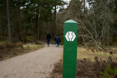 Waymarker post on the Speyside Way path with two people walking int he background.