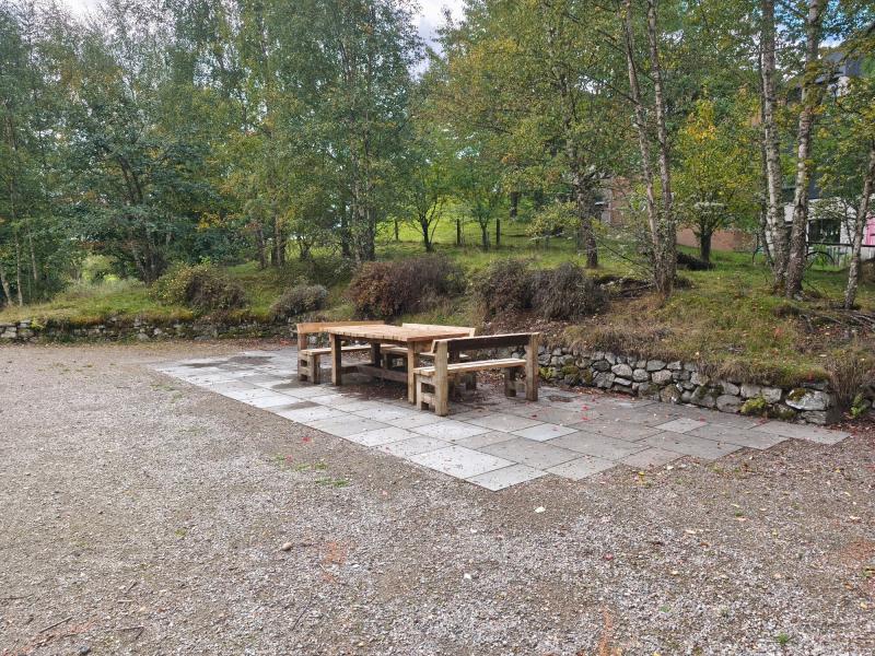 Picnic table and three benches on slabbed ground.
