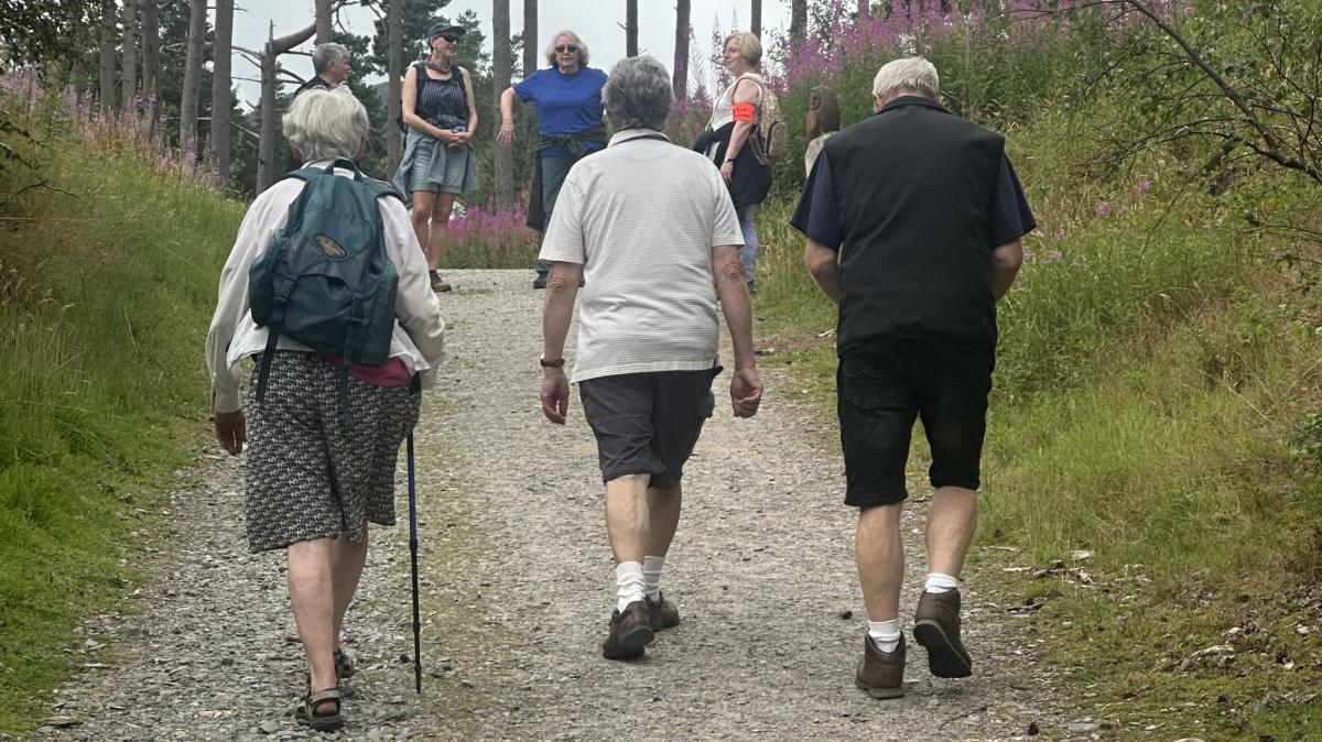 Three participants of a Health walk following fellow walkers up a path in woodland in Newtonmore.