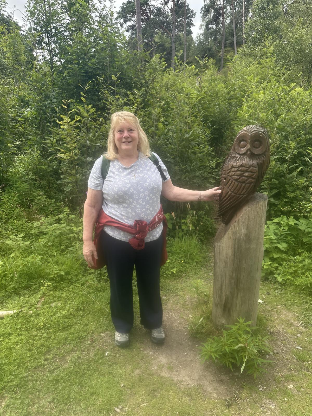 Carol standing next to a wooden carved owl.