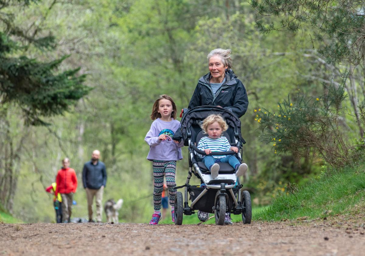A family jog with one child in a buggy, and a couple with a dog walk in the background.
