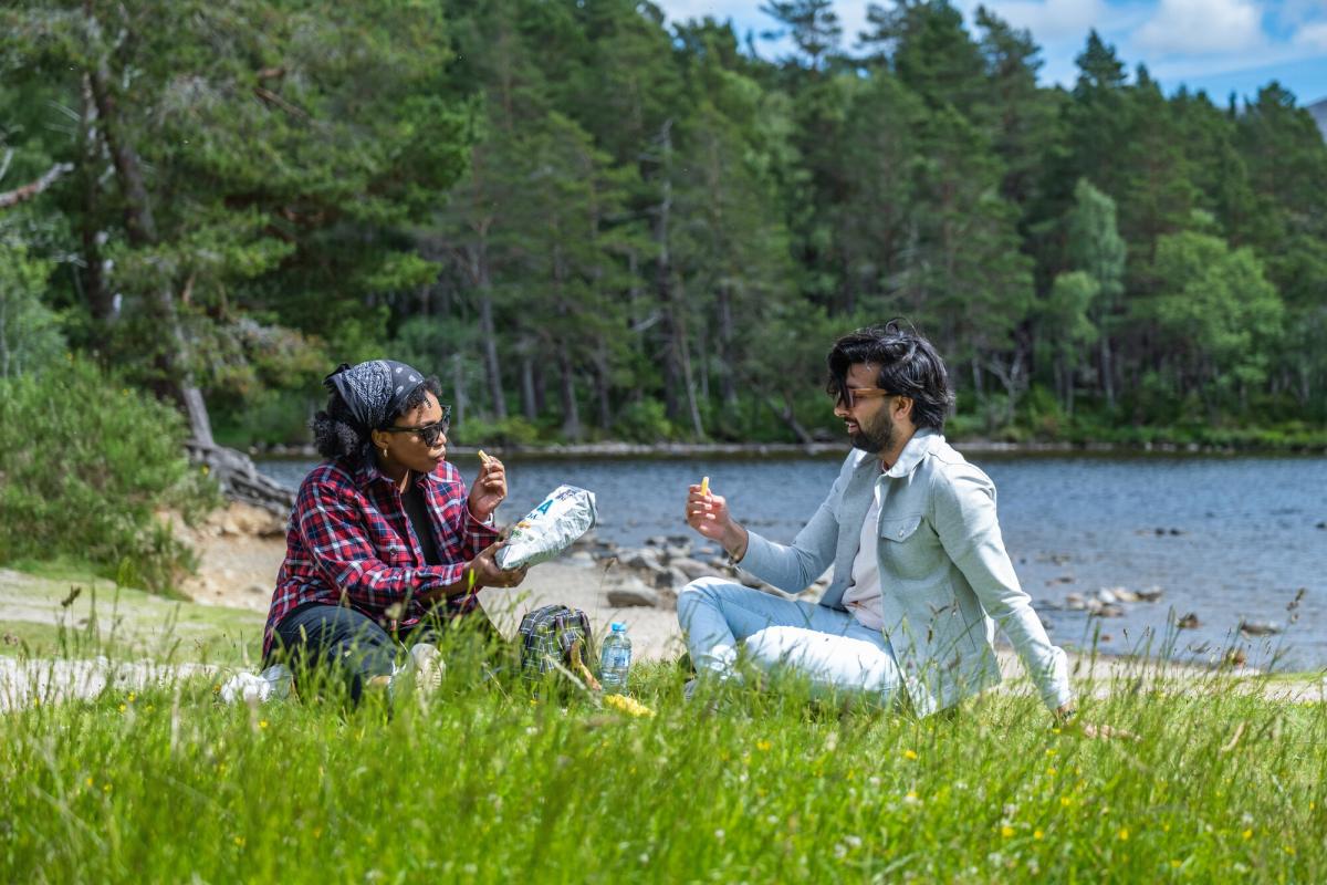 Two people having a picnic next to Loch an Eilein on a sunny day