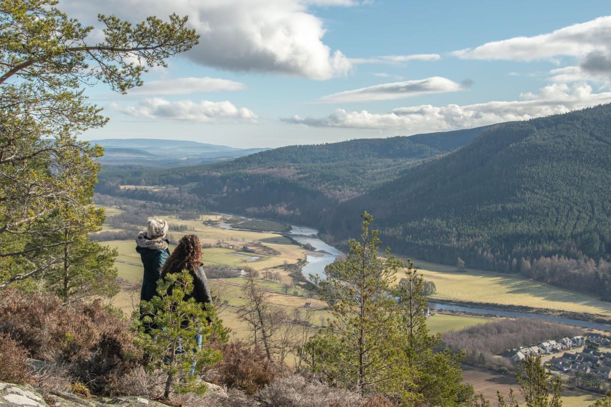 Two people admiring the view from Craigendarroch Hill overlooking Ballater and the River Dee.