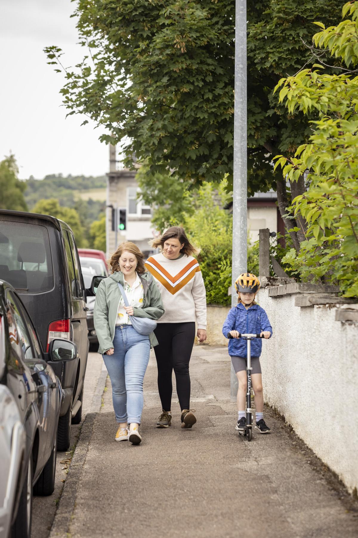 People walking down a street with a child on a scooter.