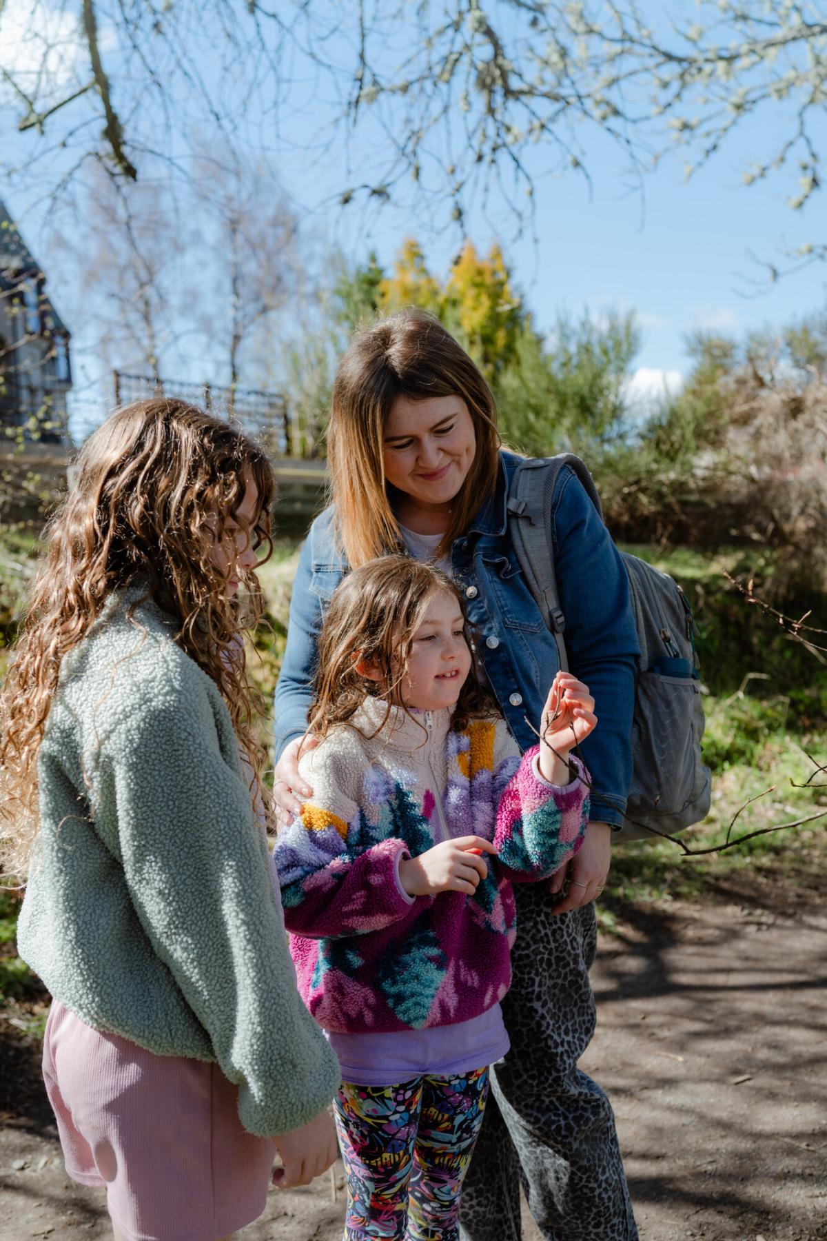 Family looking closely at new spring shoot on tree branch.