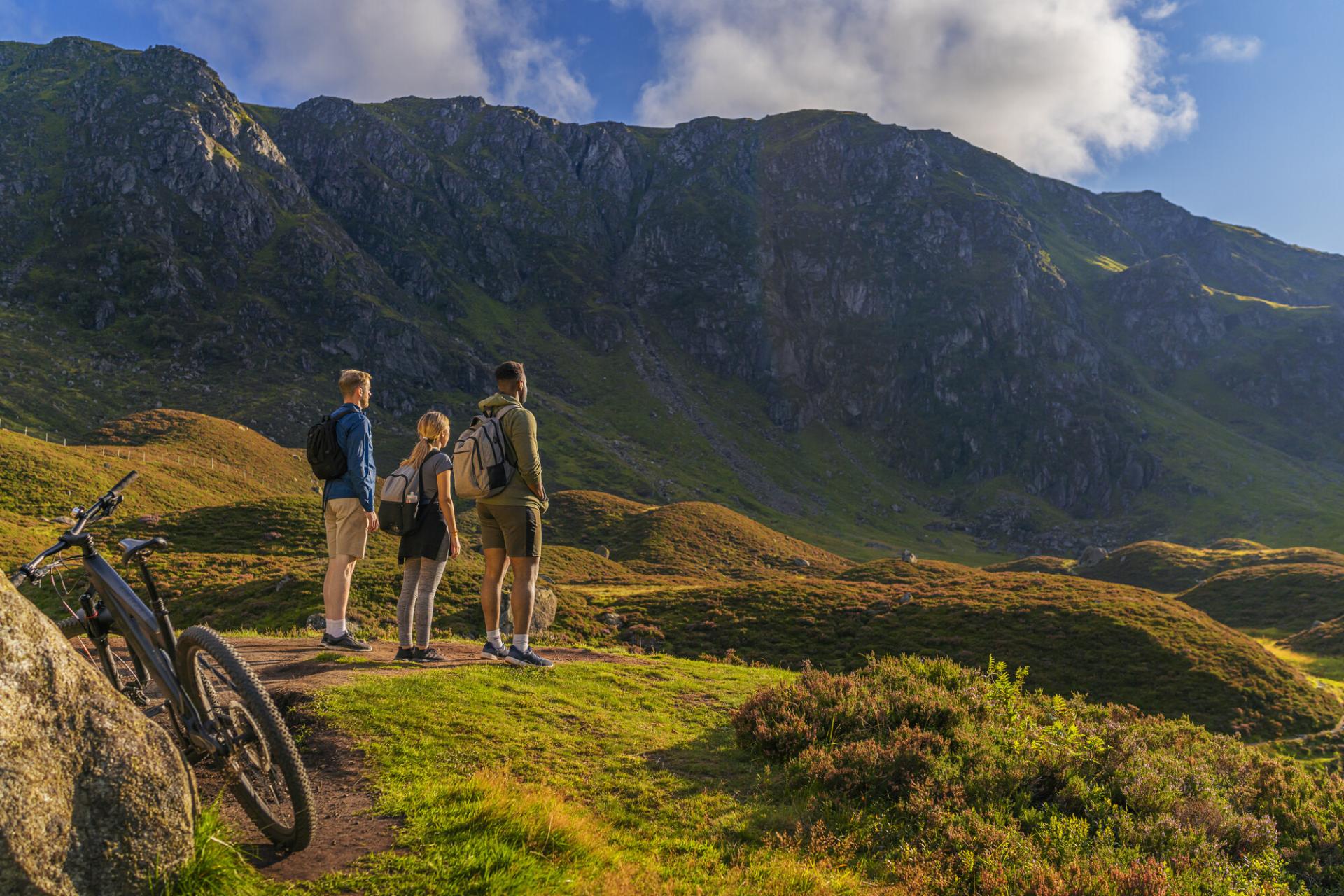 Three people admiring Corrie Fee with rugged cliffs in the background and bike in the foreground.