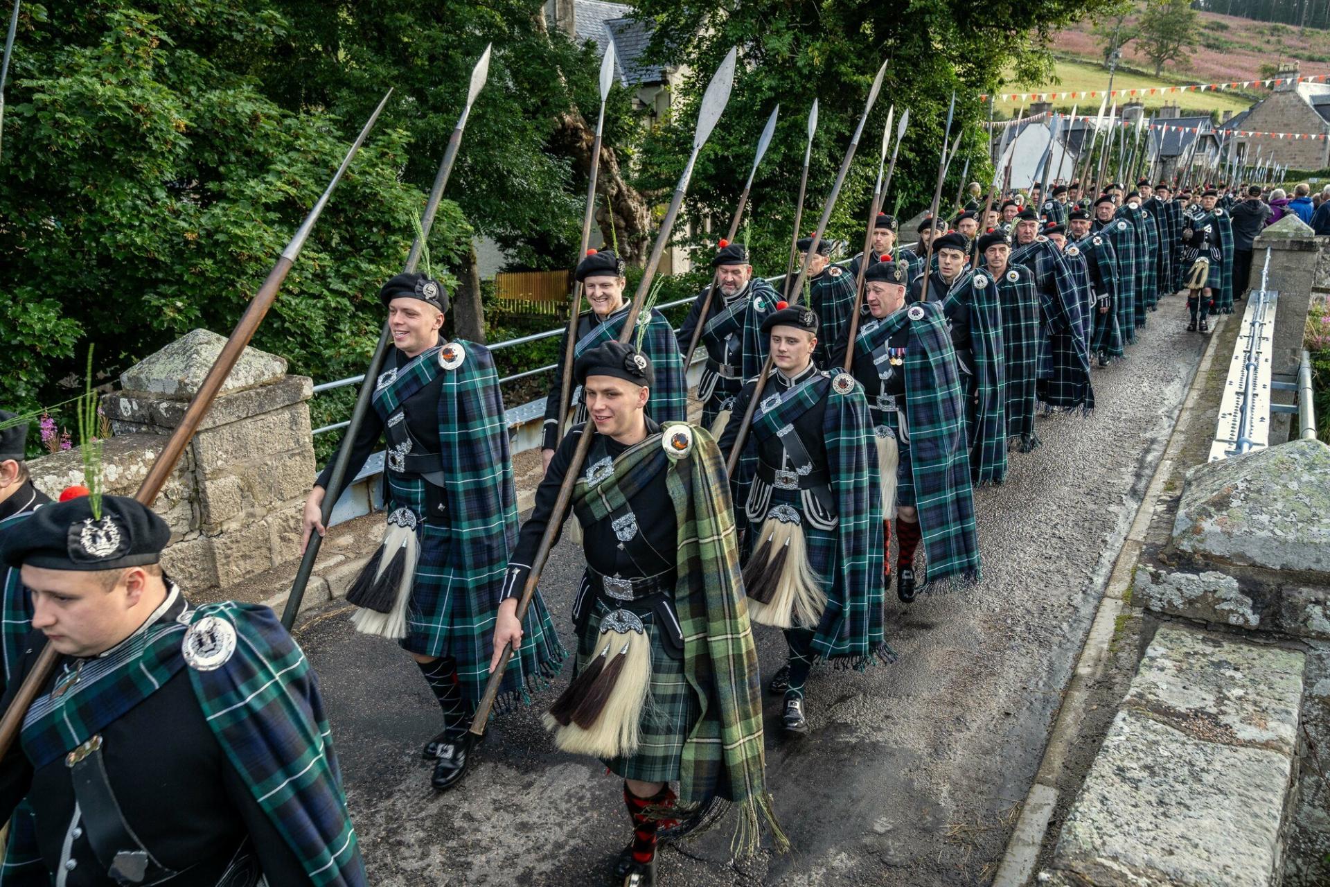 A group of marching men dressed in kilts and carrying spears