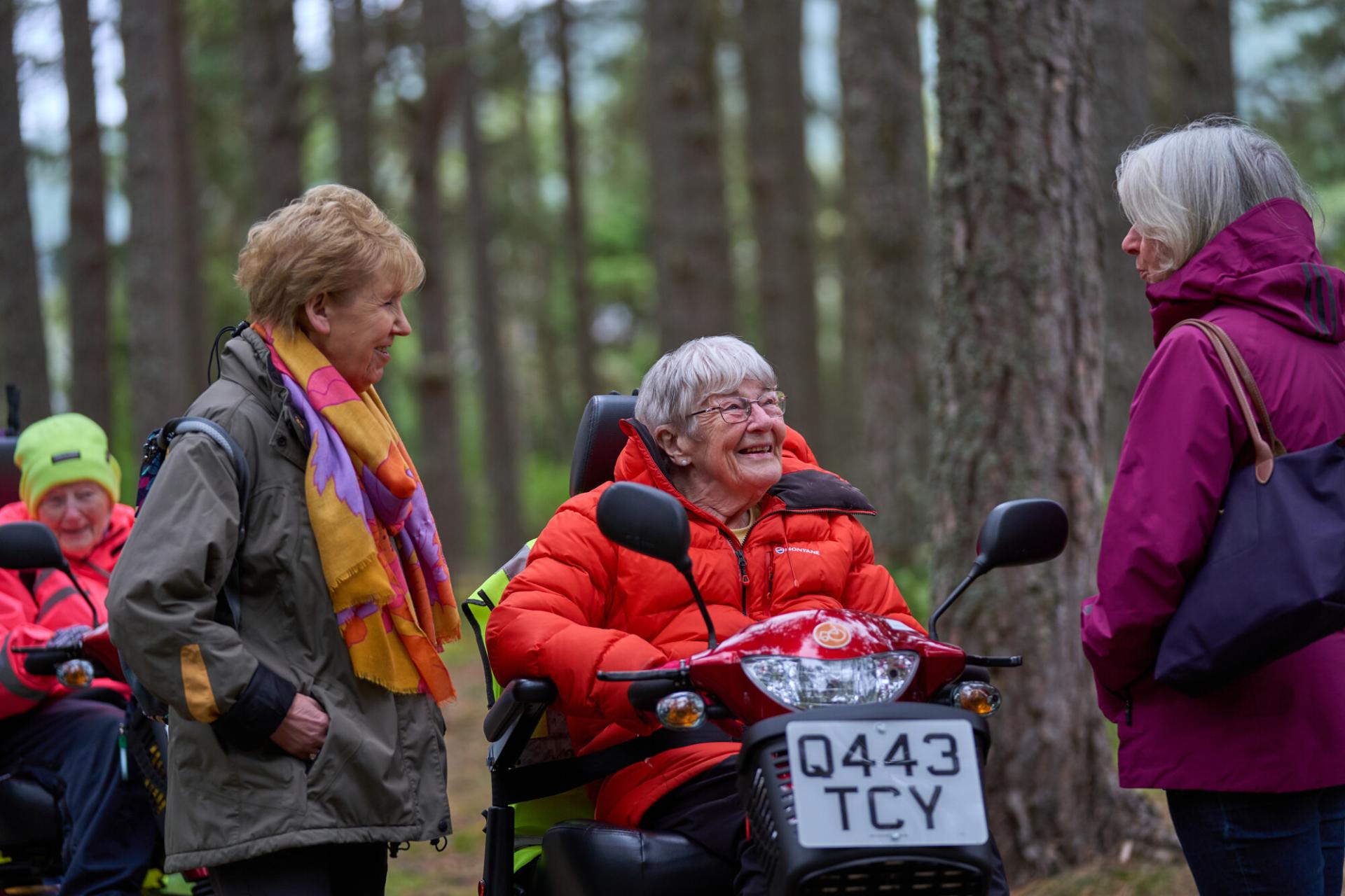 Four people in woodland, two on mobility scooters at Boat Of Garten health walk