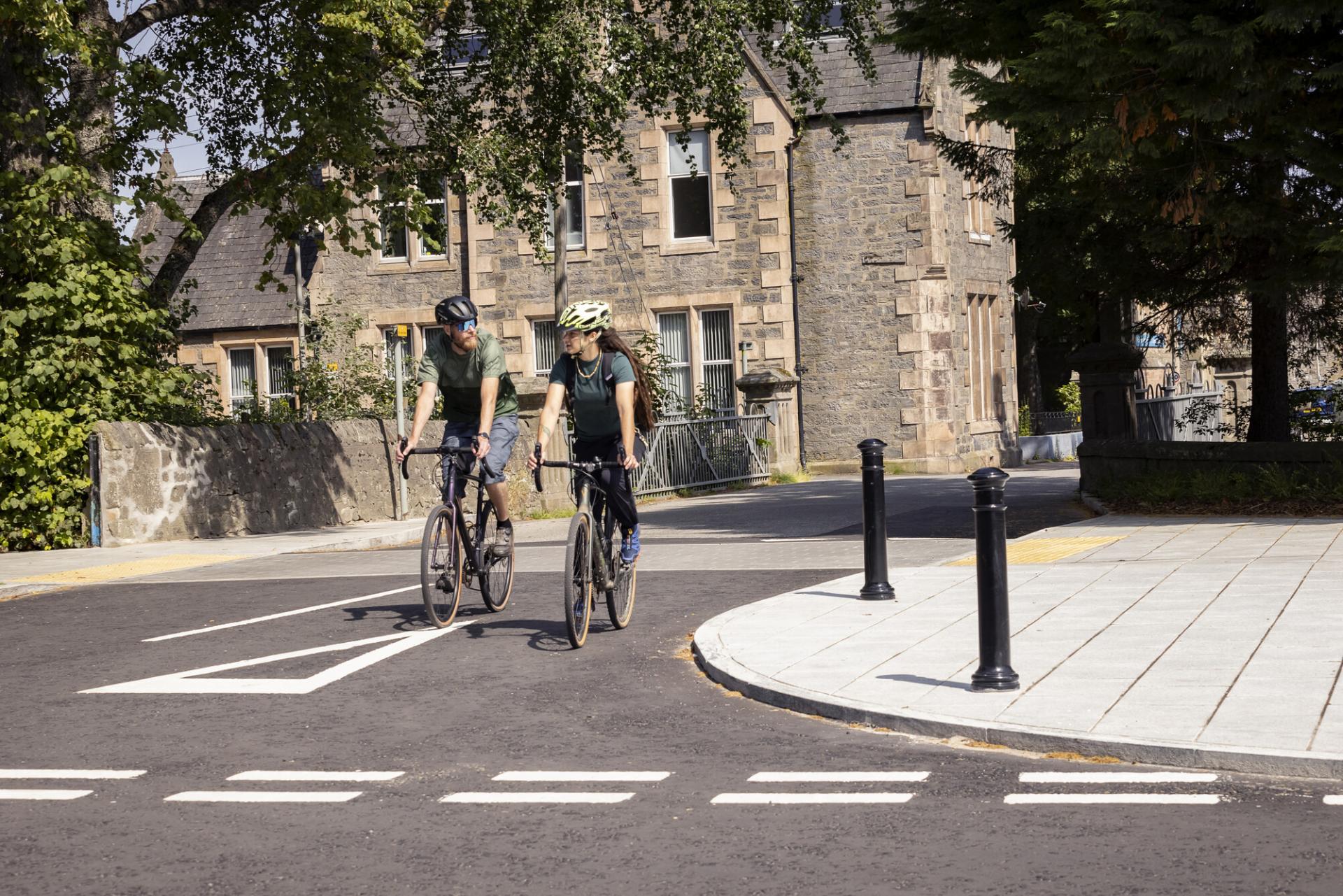 Two people riding bikes down a street approaching a junction.