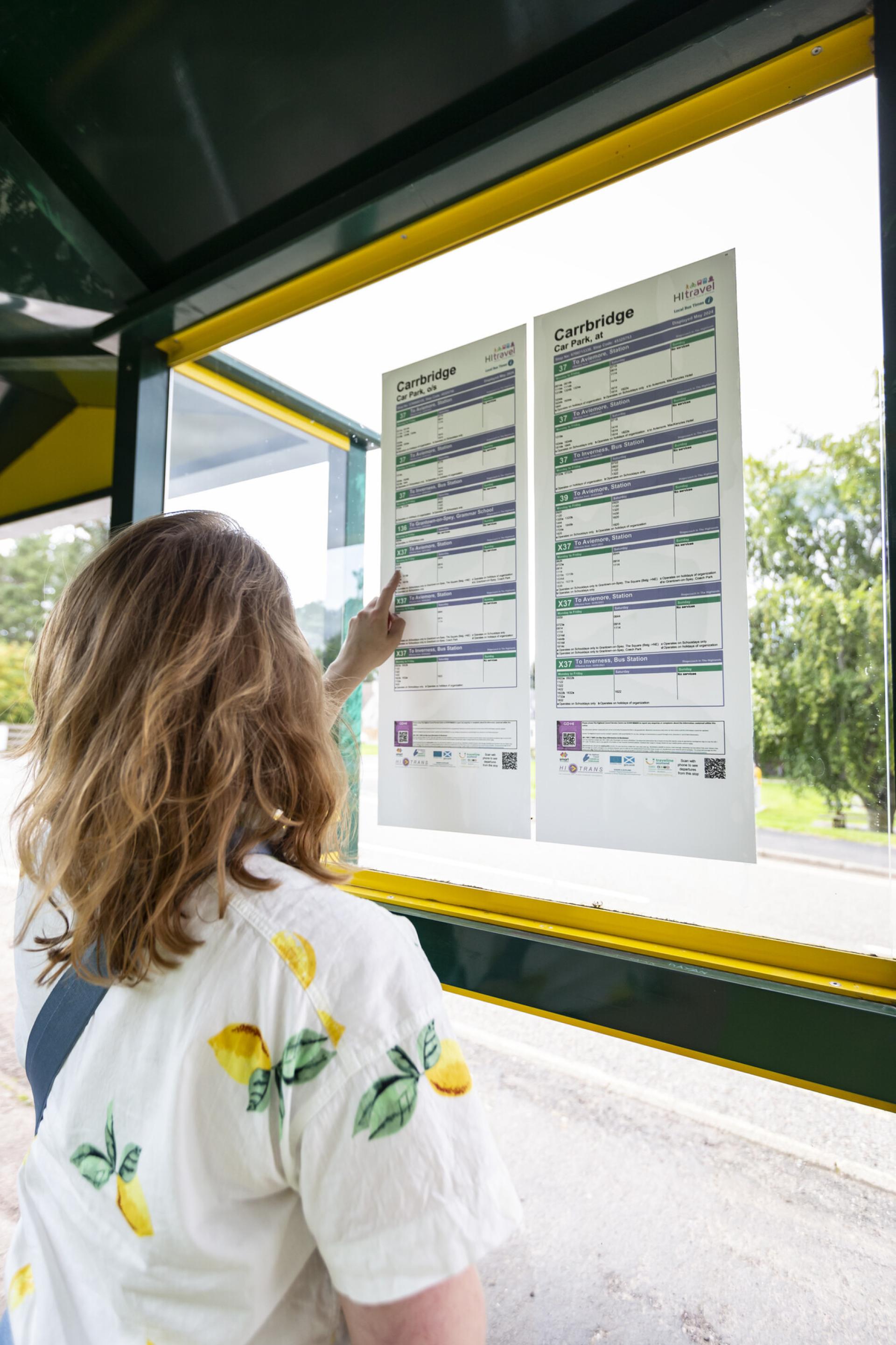 Person looking at a timetable in a bus shelter.