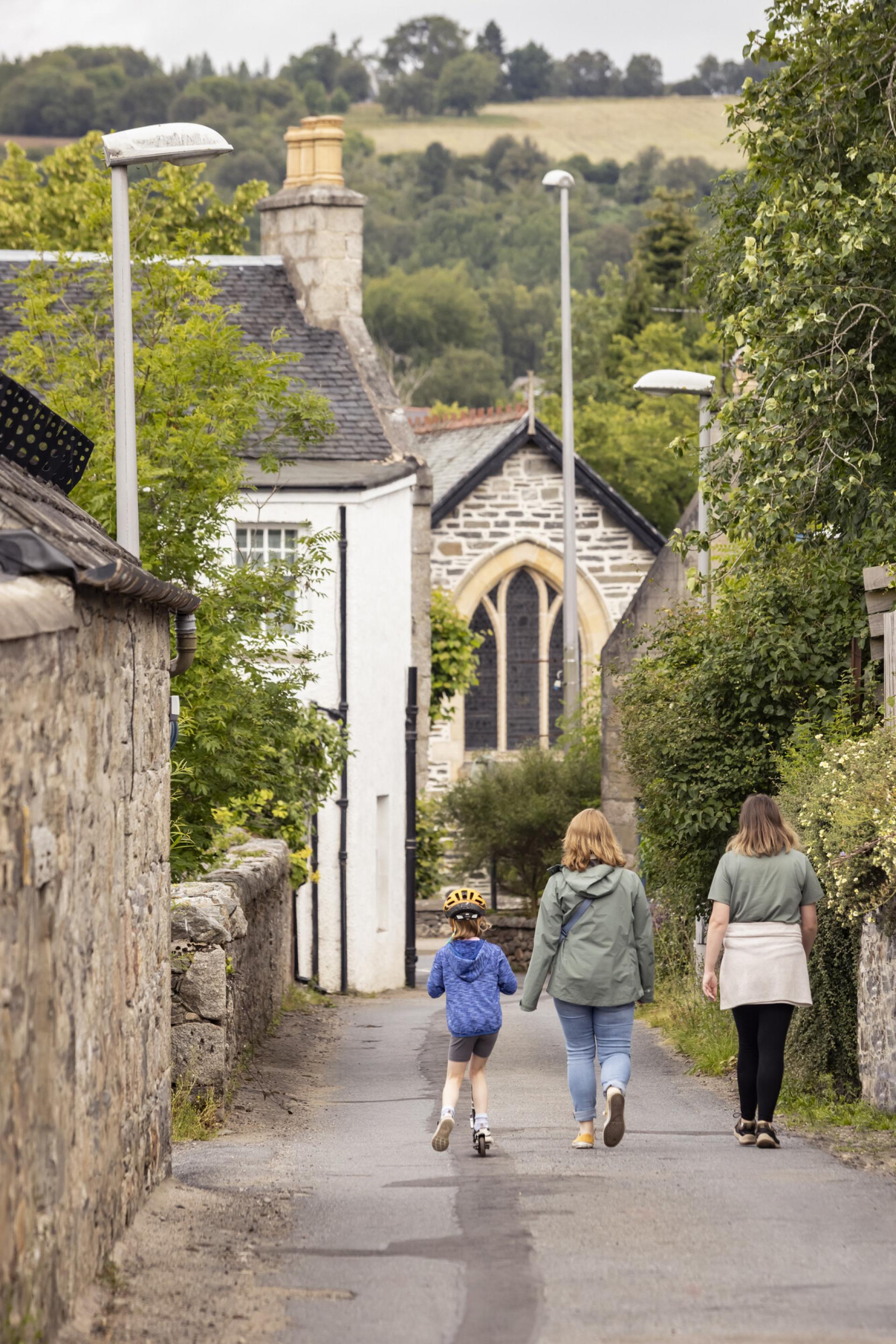 Adults walking down a road with a child on a scooter