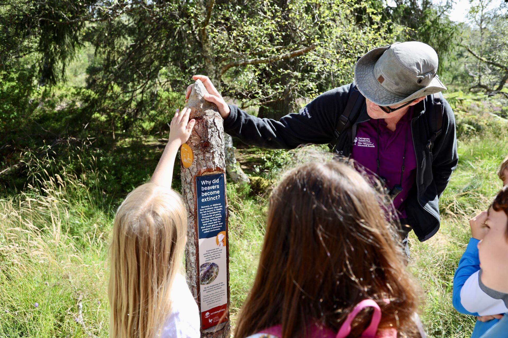 two children and one adult reading an information sign about beavers