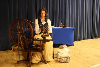 Person spinning wool, wooden floor and curtains behind the person