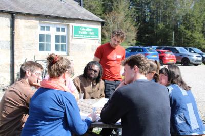 A group of eight people looking thoughtful in discussion at a picnic bench