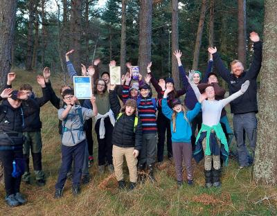 Group of junior rangers in woodland celebrating their achievement with ranger WIll George