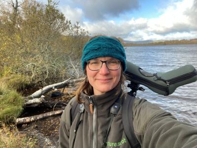 Person standing in front of a loch wearing a blue hat