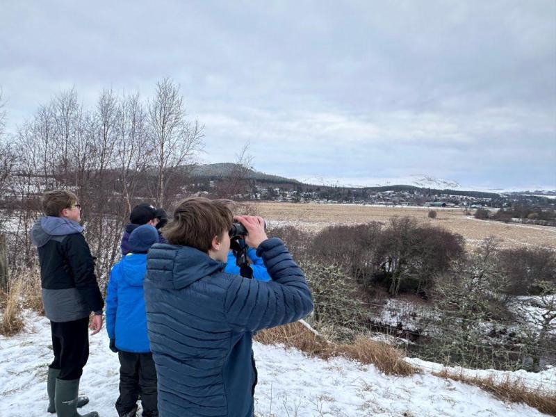 Junior Rangers looking through binoculars at a white-tailed eagle flying over moorland.