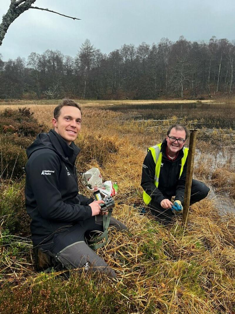 Image of Jonathan Willett and Park Authority Ranger Pete Short smiling while setting up trail cameras at the side of the loch and getting ready for the arrival of beavers.