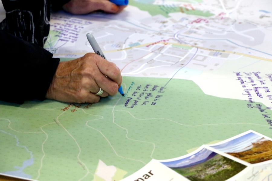 Person writing on a paper map on a table.