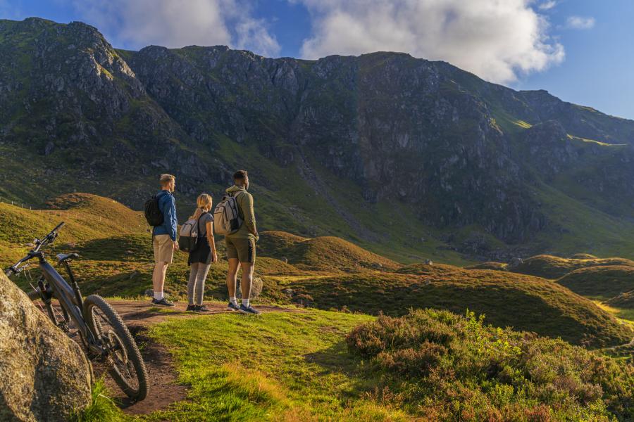 Three people admiring Corrie Fee with rugged cliffs in the background and bike in the foreground.