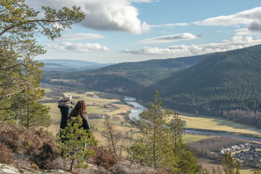 Two people admiring the view from Craigendarroch Hill overlooking Ballater and the River Dee.