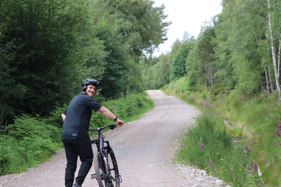 Josh Crofts walking away on woodland path with bike.
