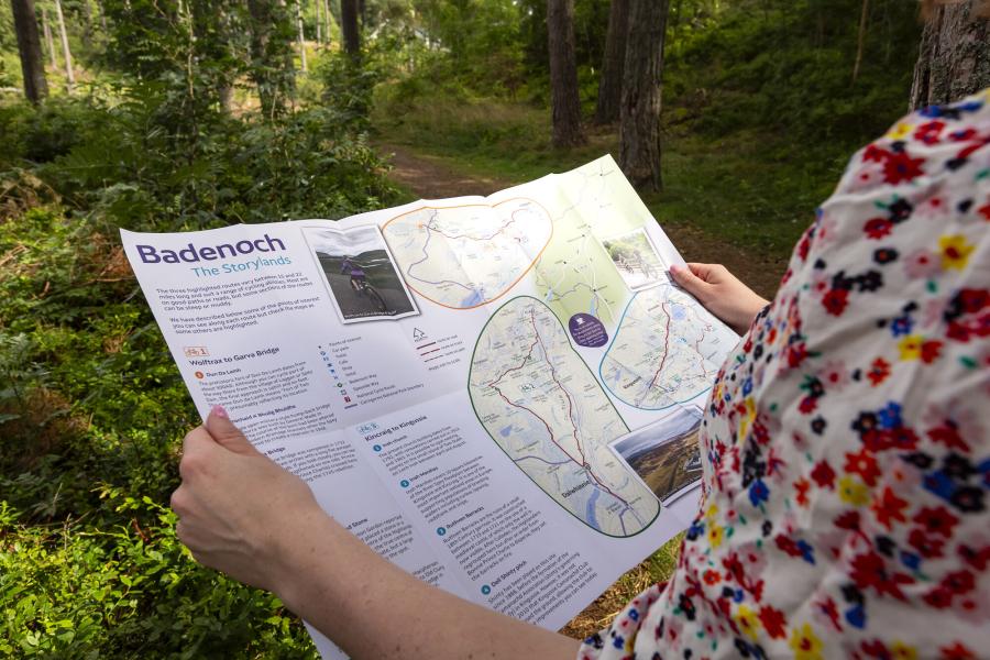 Person in woodlands holding leaflet on Badenoch The Storylands