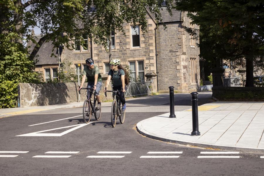 Two people riding bikes down a street approaching a junction.