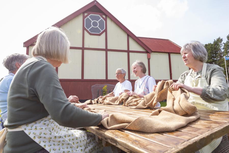 People at the Highland Folk Museum sat at an outdoor table practicing 'waulking the cloth'.