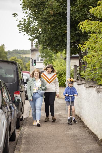 People walking down a street with a child on a scooter.
