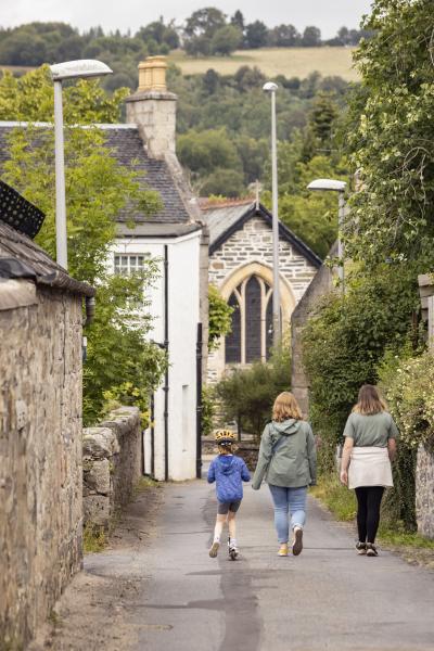 Adults walking down a road with a child on a scooter