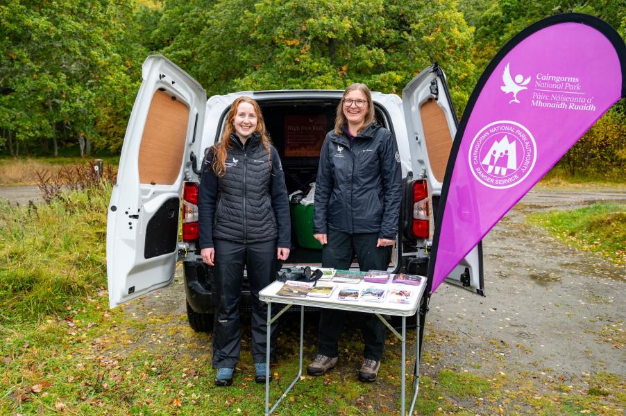 Two Deeside rangers hosting a pop-up stand, engaging with members of the public in a car park about local info, the Scottish Outdoor Access Code and the Cairngorms National Park.