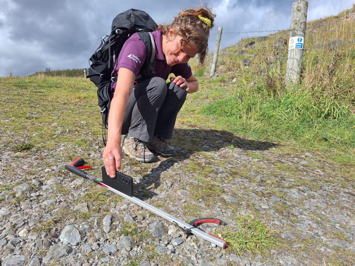 Trainee ranger Georgia smiles, balancing her phone on a litter pick to take a photo
