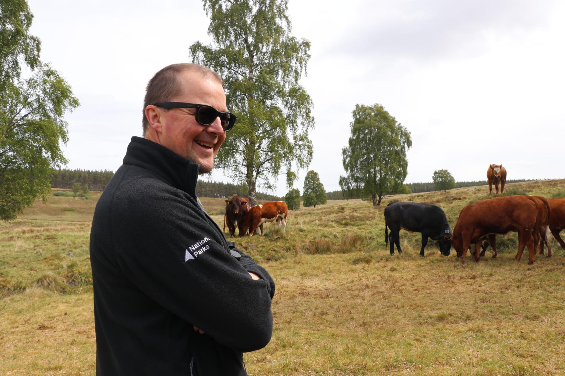 Jonathan folds his arms smiling with cows in the background