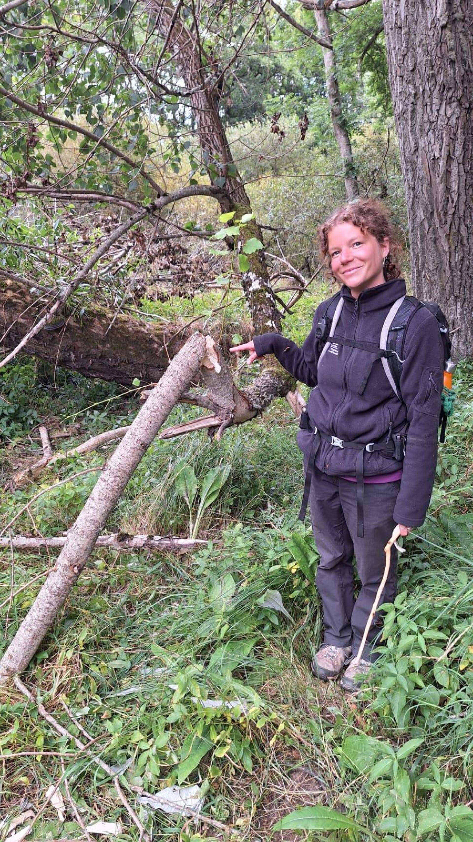 Trainee ranger Georgia stands smiling with a beaver gnawed log