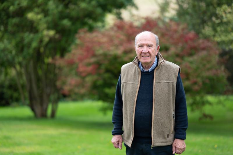 Board member Ian McLaren standing on a lawn with mature bushes in background