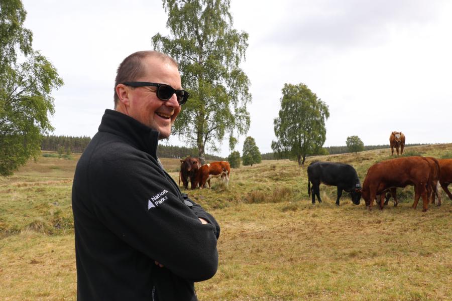 Jonathan folds his arms smiling with cows in the background
