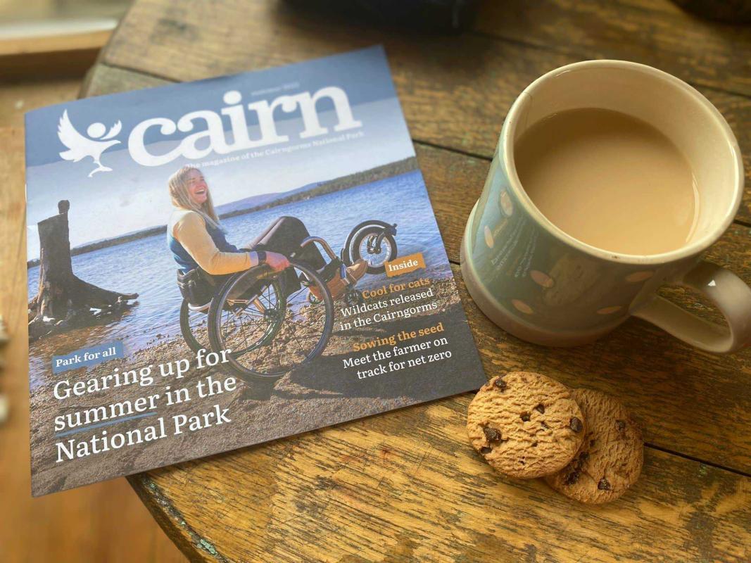 Cairn magazine on a table with a cup of tea and biscuits.