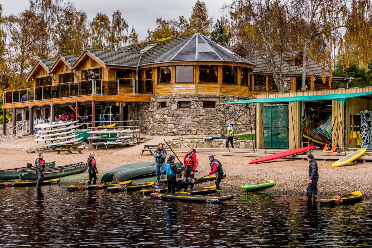 People preparing to go paddleboarding in front of Loch Insh water sports centre.