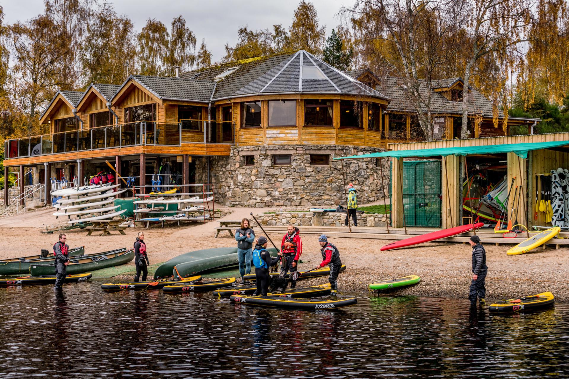 People preparing to go paddleboarding in front of Loch Insh water sports centre.