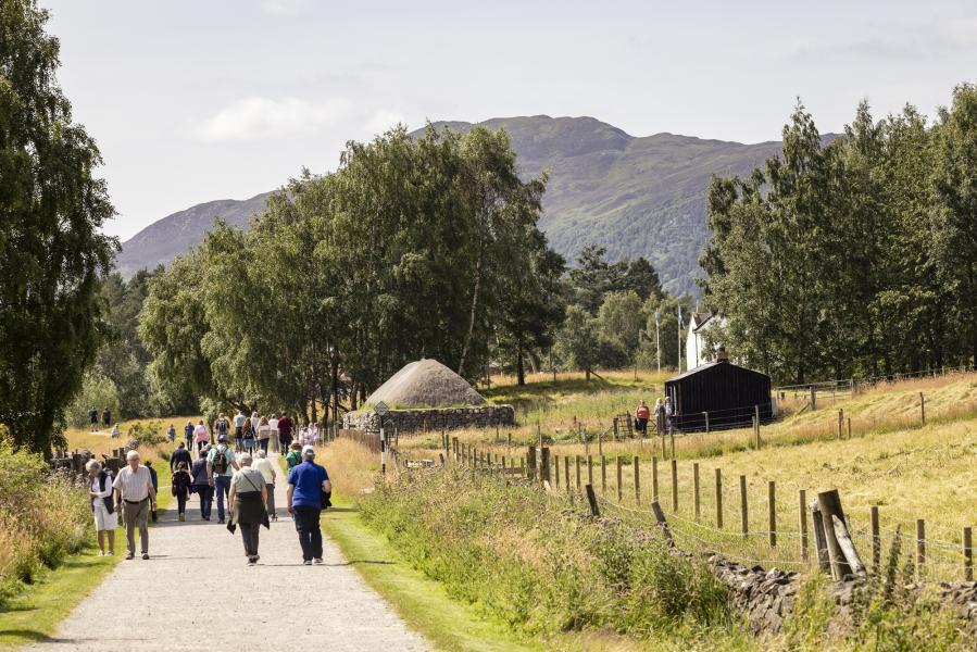 Groups of people walking on the path at the Highland Folk Museum with traditional building in the background