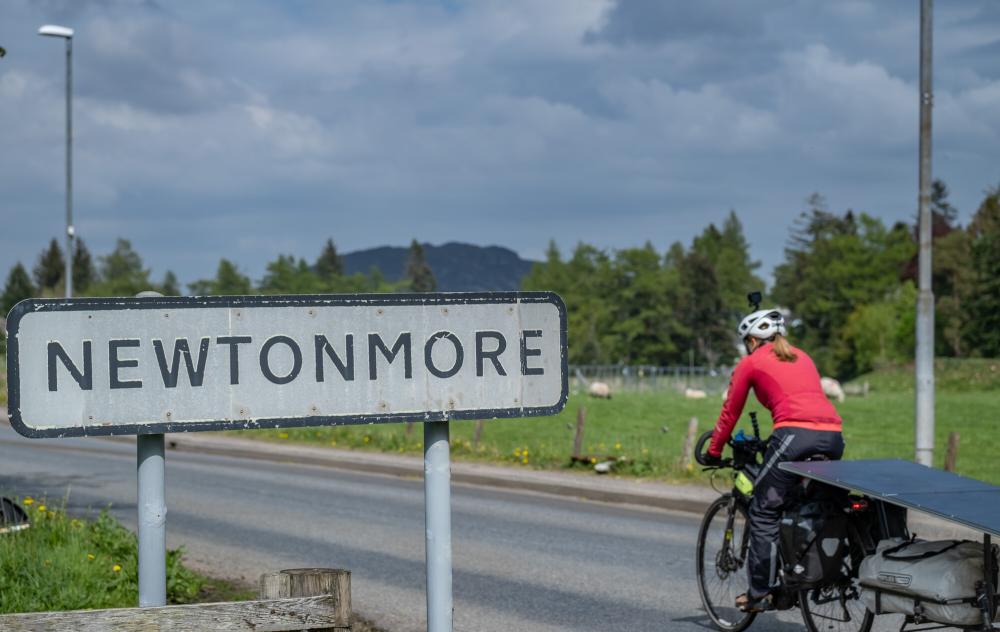 A cyclist with trailer passing the sign for Newtonmore