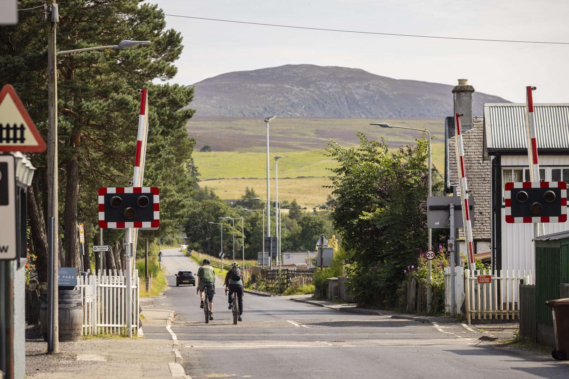 Two people cycling across Kingussie railway crossing.
