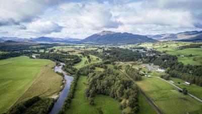 An aerial view of Newtonmore with the River Spey and mountains in the distance.