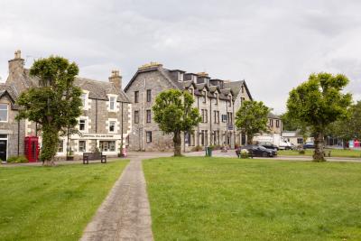 A view along a path in the village green with the Tomintoul village shop and a hotel in the background.