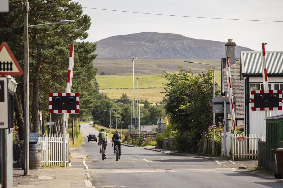 Two people cycling across Kingussie railway crossing.