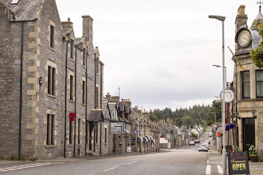 View down a Tomintoul street featuring the Richmond Arms Hotel and Clockhouse restaurant with trees in far background.
