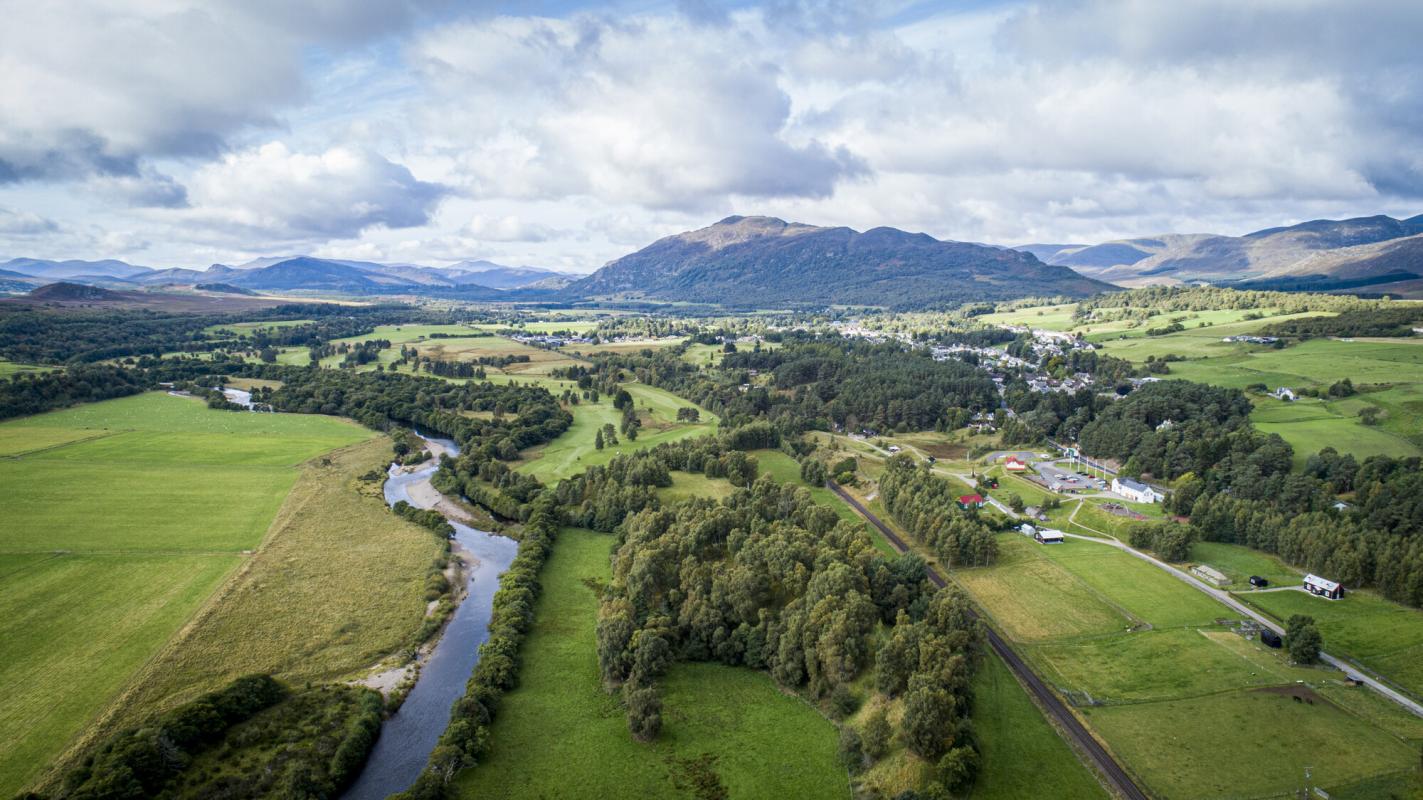 An aerial view of Newtonmore with the River Spey and mountains in the distance.